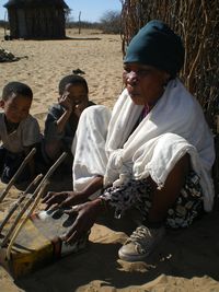 Oba plays the zhoma (pluriarc) while children look on.