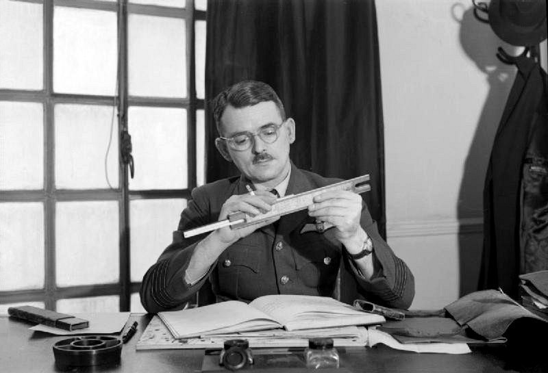 Frank Whittle adjusts a slide rule while seated at his desk at the Ministry of Aircraft Production